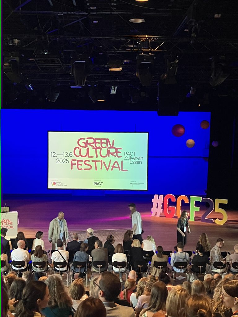 Es ist eine Präsentation zu sehen, auf der "Green Culture Festival" zu lesen ist. Es sind viele Menschen anwesend. Es ist die Eröffnung des Green Culture Festivals.