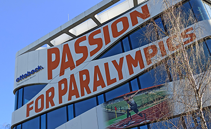 Das Foto zeigt den Schriftzug Passion for Paralympics an einer Gebäudefassade eines Herstellers für Prothesen und anderen orthopädischen Hilfen und Hilfsgeräten. Das Foto wurde bei strahlendem Sonnenschein vor einem wolkenlosen blauen Himmel in Berlin aufgenommen. 